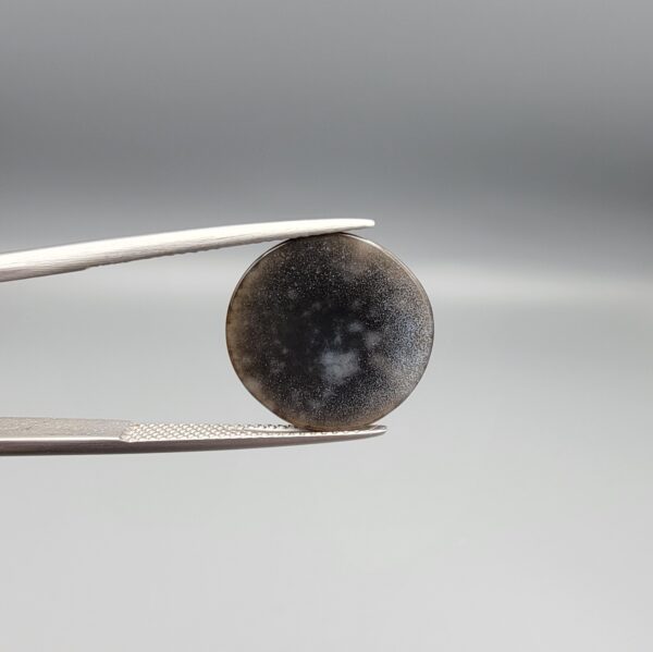 Multi-angle macro photographs of a 10.47-carat natural African Banded Eye Agate (Sulemani Aqeeq) shown in gem tweezers and on fingertips, featuring a high round cabochon dome with concentric black, brown, and white fortification rings framing a luminous pale blue-grey eye core, parallel layered profile banding, and a dark mottled reverse base with a nebulous center.