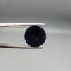 Multi-angle macro photographs of a 7.14-carat natural African Banded Eye Agate (Sulemani Aqeeq) shown in gem tweezers and on fingertips, featuring a high round cabochon dome with a deep black body accented by a sharp teardrop-shaped concentric white and black ring pattern forming a distinct central eye motif, and a solid uniform black reverse base with minor edge wear.
