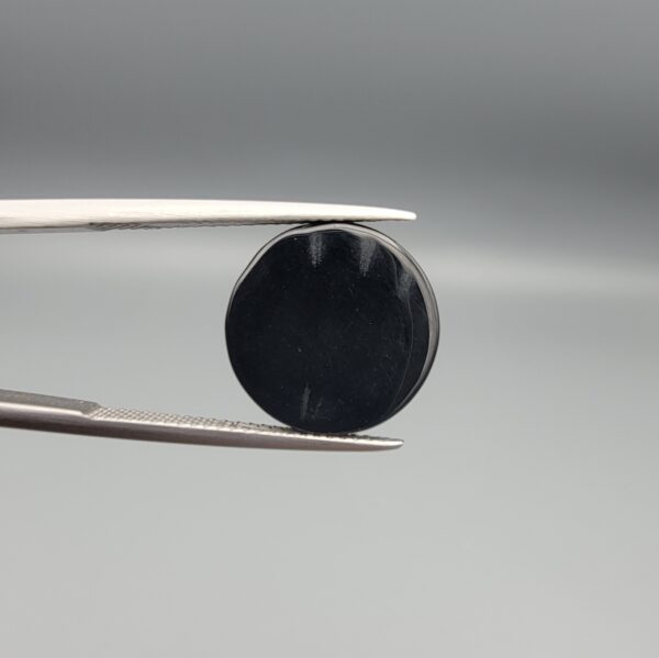 Multi-angle macro photographs of a 9.85-carat natural African Banded Eye Agate (Sulemani Aqeeq) held in gem tweezers, featuring a top view with a central eye motif of concentric white and dark rings set in a deep black body, a profile view demonstrating smooth high-dome geometry and layered fortification banding, and a reverse view of a flat solid black base.