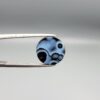 Multi-angle macro photographs of a 5.97-carat natural African Banded Eye Agate (Sulemani Aqeeq) held in gem tweezers, showing a top view with a dominant black body framed by a sharp white arc, a profile view with a distinct V-shaped white fortification band, and a reverse view revealing a multi-eye cellular pattern in blue-grey and black.