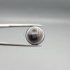 Multi-angle macro photographs of a 12.13-carat natural African Banded Eye Agate (Sulemani Aqeeq) held in steel gem tweezers, showcasing a top view with concentric white and dark brown fortification bands surrounding a translucent core with a dark eye inclusion, a profile view displaying layered fortification banding, and a reverse view revealing multiple rounded eye motifs and cellular banding against a dark chalcedony field.