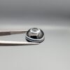 Multi-angle macro photographs of a 6.29-carat natural African Banded Eye Agate (Sulemani Aqeeq) held in steel gem tweezers, showcasing a top view with a central black pupil enclosed by a crisp white halo ring, a profile view displaying lower flank fortification bands, and a reverse view revealing a flat translucent milky-grey gradient base.