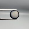 Multi-angle macro photographs of a 6.29-carat natural African Banded Eye Agate (Sulemani Aqeeq) held in steel gem tweezers, showcasing a top view with a central black pupil enclosed by a crisp white halo ring, a profile view displaying lower flank fortification bands, and a reverse view revealing a flat translucent milky-grey gradient base.