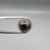 Multi-angle macro photographs of a 9.53-carat natural African Banded Eye Agate (Sulemani Aqeeq) held in steel gem tweezers, showcasing a top view with a translucent brownish-grey central field framed by a sharp concentric ring, a side profile revealing layered fortification banding along the flanks, and a smooth jet-black flat reverse base.
