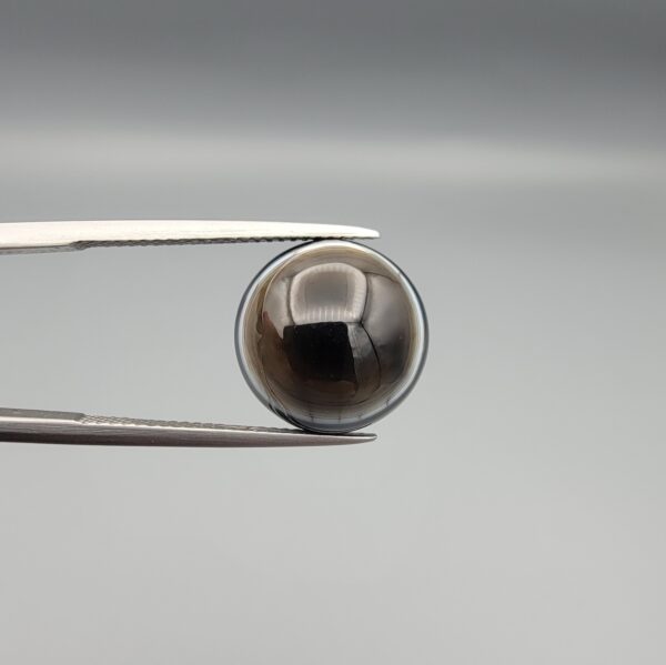 Multi-angle macro photographs of a 9.53-carat natural African Banded Eye Agate (Sulemani Aqeeq) held in steel gem tweezers, showcasing a top view with a translucent brownish-grey central field framed by a sharp concentric ring, a side profile revealing layered fortification banding along the flanks, and a smooth jet-black flat reverse base.