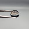 Multi-angle macro photographs of a 9.53-carat natural African Banded Eye Agate (Sulemani Aqeeq) held in steel gem tweezers, showcasing a top view with a translucent brownish-grey central field framed by a sharp concentric ring, a side profile revealing layered fortification banding along the flanks, and a smooth jet-black flat reverse base.