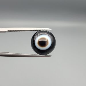 Multi-angle macro photographs of a 6.20-carat natural African Banded Eye Agate (Sulemani Aqeeq) held in steel gem tweezers, displaying a top view with a deep black core enclosed by a sharp concentric white ring, a side profile revealing smooth high-dome curvature, and a reverse view featuring a flat, solid black base with subtle natural mineral matrix markings.