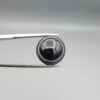 Multi-angle macro photographs of an 8.57-carat natural African Banded Eye Agate (Sulemani Aqeeq) held in steel gem tweezers, showcasing a top view with a crisp concentric outer white ring framing a deep black core, a side profile displaying high-dome geometry and layered fortification pinstripes, and a reverse view of a flat, solid mirror-polished black base.