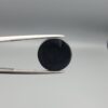 Multi-angle macro photographs of an 8.57-carat natural African Banded Eye Agate (Sulemani Aqeeq) held in steel gem tweezers, showcasing a top view with a crisp concentric outer white ring framing a deep black core, a side profile displaying high-dome geometry and layered fortification pinstripes, and a reverse view of a flat, solid mirror-polished black base.