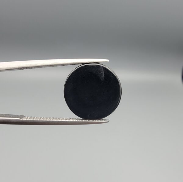 Multi-angle macro photographs of an 8.57-carat natural African Banded Eye Agate (Sulemani Aqeeq) held in steel gem tweezers, showcasing a top view with a crisp concentric outer white ring framing a deep black core, a side profile displaying high-dome geometry and layered fortification pinstripes, and a reverse view of a flat, solid mirror-polished black base.