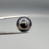 Multi-angle macro photographs of a 7.64-carat natural African Banded Eye Agate (Sulemani Aqeeq) held in steel gem tweezers, showcasing a top view with a sharp concentric ring and lower translucent band, a side profile displaying smooth high-dome geometry with horizontal flank fortification, and a reverse view of a flat black base featuring a striking horizontal banded division.