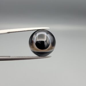 Multi-angle macro photographs of a 7.64-carat natural African Banded Eye Agate (Sulemani Aqeeq) held in steel gem tweezers, showcasing a top view with a sharp concentric ring and lower translucent band, a side profile displaying smooth high-dome geometry with horizontal flank fortification, and a reverse view of a flat black base featuring a striking horizontal banded division.