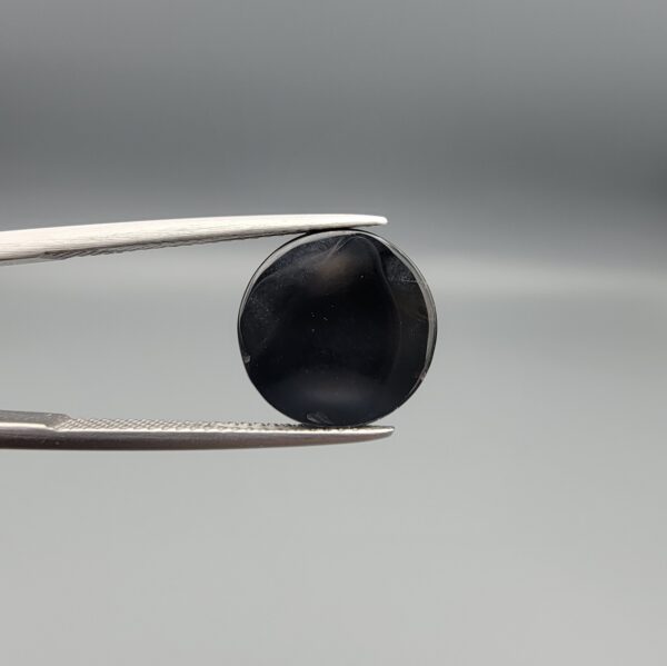 Multi-angle macro photographs of a 5.89-carat natural African Banded Eye Agate (Sulemani Aqeeq) held in steel gem tweezers, displaying a top view with a crisp concentric white ring framing a dark brownish-black central core, and a reverse view revealing a flat, dark mottled chalcedony base with subtle natural edge inclusions.