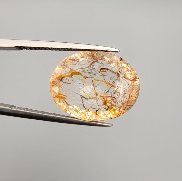 High-resolution macro photographs of a 17.27-carat natural Rutilated Quartz (Moh-e-Najaf) held in steel tweezers, displaying a finely faceted oval silhouette, water-clear crystal body, and rich internal golden-brown hematite platelets with contrasting dark rutile needles sourced from Najaf Al-Ashraf, Iraq.