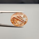 High-resolution macro photographs of an 8.99-carat natural Rutilated Quartz (Moh-e-Najaf) held in steel tweezers, showcasing a masterfully faceted oval silhouette, water-clear quartz body, and striking diagonal reddish-brown rutile blade inclusions sourced from Najaf Al-Ashraf, Iraq.