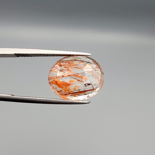 High-resolution macro photographs of an 8.52-carat natural Rutilated Quartz (Moh-e-Najaf) held in steel tweezers, showcasing a brilliant oval facet cut, exceptional crystal clarity, and a dynamic internal weave of coppery orange-red hematite platelets interspersed with fine rutile needles sourced from Najaf Al-Ashraf, Iraq.
