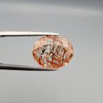 High-resolution macro photographs of a 7.20-carat natural Rutilated Quartz (Moh-e-Najaf) held in steel tweezers, displaying a brilliant oval facet cut, water-clear crystal clarity, and a dramatic internal network of crisscrossing copper-red blades with contrasting dark rutile needles sourced from Najaf Al-Ashraf, Iraq.