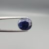 High-resolution macro photographs of a 5.40-carat natural Afghan Blue Indigo Sapphire (Neelam) held in steel gem tweezers, showcasing a masterfully faceted oval silhouette, deep midnight indigo-blue body color, and natural internal corundum silk structures sourced from Afghanistan.