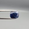High-resolution macro photographs of a 7.31-carat natural Afghan Blue Indigo Sapphire (Neelam) held in steel gem tweezers, showcasing a soft cushion facet cut, deep indigo-blue body color, and natural internal corundum silk structures sourced from Afghanistan.