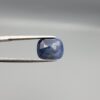 High-resolution macro photographs of a 7.31-carat natural Afghan Blue Indigo Sapphire (Neelam) held in steel gem tweezers, showcasing a soft cushion facet cut, deep indigo-blue body color, and natural internal corundum silk structures sourced from Afghanistan.