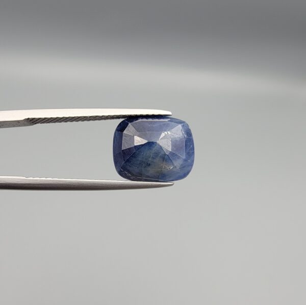 High-resolution macro photographs of a 7.31-carat natural Afghan Blue Indigo Sapphire (Neelam) held in steel gem tweezers, showcasing a soft cushion facet cut, deep indigo-blue body color, and natural internal corundum silk structures sourced from Afghanistan.