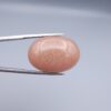 High-resolution macro photographs of a 34.71-carat natural Sunstone (Sang-e-Aftabi) held in steel tweezers, showcasing a smooth oval cabochon cut, warm peach-orange matrix, and dense aventurescent metallic specks that create a brilliant shimmering schiller effect.