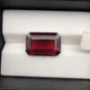 High-resolution macro photographs of an 11.32-carat natural Hessonite Garnet (Gomed) displayed on a white textured leather cushion inside a black display box, showcasing a precision emerald step-cut rectangular silhouette, rich deep reddish-brown to warm cinnamon-amber hues, and signature internal heat-wave transparency (treacle effect).