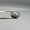 High-resolution macro photographs showing a 10.04-carat natural Serpentine (Zehr Mora) oval cabochon held in gemological tweezers from front and back views, displaying a striking bicolor division of sage-green matrix and deep black mineral bands under a high-luster polished dome.