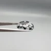 High-resolution macro photographs showing a 13.78-carat natural Serpentine (Zehr Mora) oval cabochon held in tweezers and showcased on hand, displaying a deep jet-black base matrix contrasting with crisp white snowflake-like inclusions under a high-luster polished dome.
