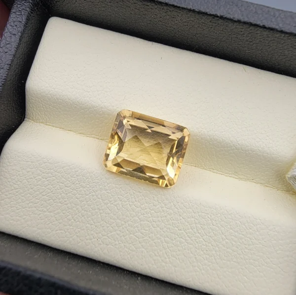 High-resolution macro photograph displaying a 4.42-carat natural Citrine Quartz (Sunela) octagon step cut gemstone resting in a white display box, showcasing crisp emerald-cut step facets, high transparency, and a refined golden-yellow color.