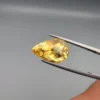 High-resolution macro photographs showing a 6.57-carat natural Citrine Quartz (Sunela) pear cut faceted gemstone in a white-padded display box and held in gemological tweezers, exhibiting brilliant golden-yellow color, high crystal transparency, and crisp precision faceting.