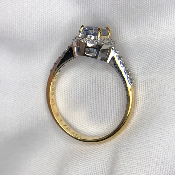​Close-up top-down photograph of an 18k gold diamond halo ring featuring a 1.72-carat natural pastel blue Ceylon sapphire (Neelam) accented by 0.33 carats of brilliant pavé diamonds, presented on a soft white fabric background.