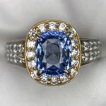 Macro photograph of a sterling silver statement ring featuring a magnificent 4.00-carat cushion-cut natural Ceylon blue sapphire center stone enclosed by a brilliant halo of accent stones and pavé shoulders against a white background.