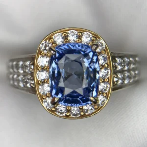 Macro photograph of a sterling silver statement ring featuring a magnificent 4.00-carat cushion-cut natural Ceylon blue sapphire center stone enclosed by a brilliant halo of accent stones and pavé shoulders against a white background.
