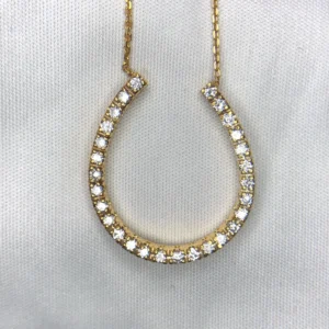 Macro photographs of a 14K yellow gold horseshoe diamond pendant necklace held against a white fabric backdrop, featuring 0.42 carats of natural round brilliant-cut diamonds prong-set along the horseshoe arch on a delicate gold chain.