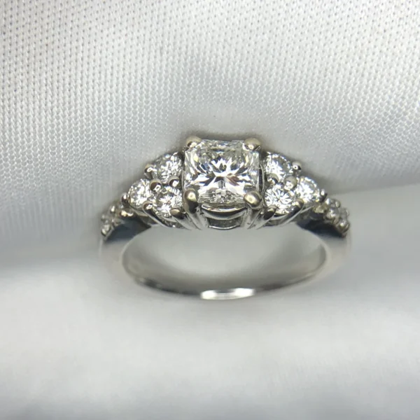 Multi-angle macro photographs of a 14K white gold 7-stone diamond engagement ring held against a white fabric backdrop, featuring a central natural cushion-cut diamond flanked by six graduated round brilliant-cut diamonds across the gallery band.