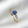 Macro photograph of a 1.91-gram 18K yellow gold fine ring set with a central 0.68-carat vibrant royal blue Ceylon sapphire flanked by sparkling diamond accents (0.04 CTW) on marquise-style shoulder settings against a white background.