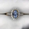 ​Close-up top-down photograph of an 18k gold diamond halo ring featuring a 1.72-carat natural pastel blue Ceylon sapphire (Neelam) accented by 0.33 carats of brilliant pavé diamonds, presented on a soft white fabric background.