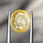 Studio close-up photograph showcasing a 6.63-carat natural trapiche yellow sapphire Pukhraj gemstone with a distinct wheel-like growth pattern, held securely in precision tweezers.