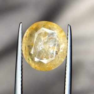 Studio close-up photograph showcasing a 6.63-carat natural trapiche yellow sapphire Pukhraj gemstone with a distinct wheel-like growth pattern, held securely in precision tweezers.