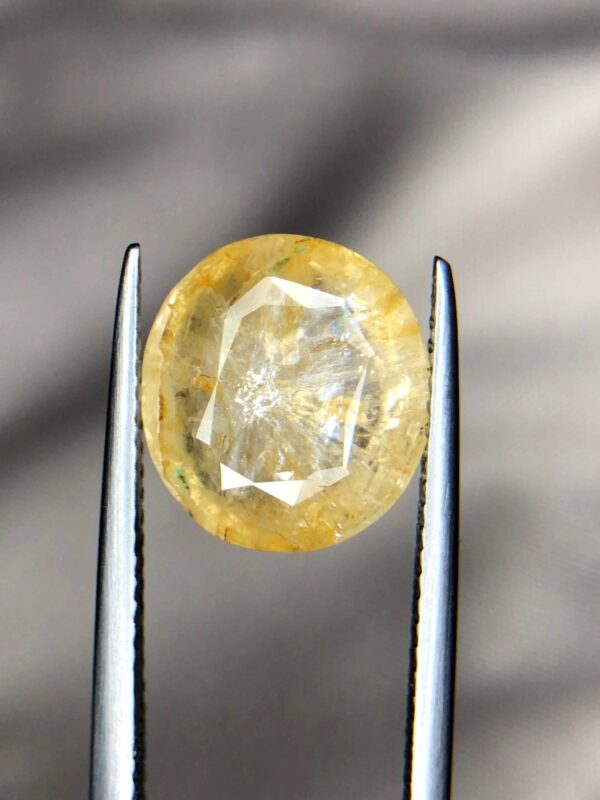 Studio close-up photograph showcasing a 6.63-carat natural trapiche yellow sapphire Pukhraj gemstone with a distinct wheel-like growth pattern, held securely in precision tweezers.