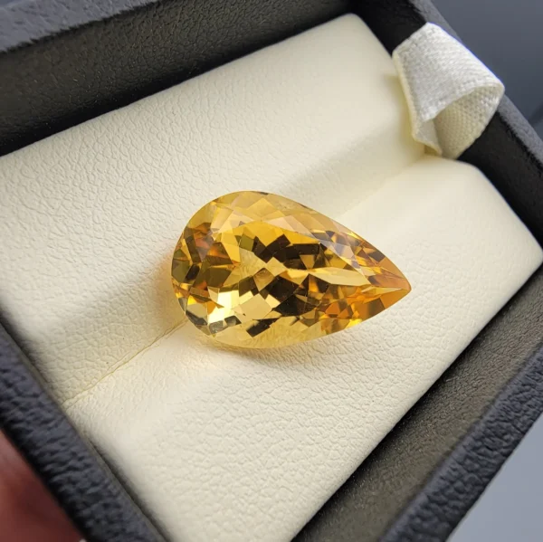 High-resolution macro photographs showing an 8.32-carat natural Citrine Quartz (Sunela) pear cut faceted gemstone set in a white display box, showcasing intense golden-amber saturation, eye-clean clarity, and brilliant light dispersion.