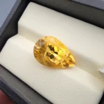 High-resolution macro photographs showing an 8.32-carat natural Citrine Quartz (Sunela) pear cut faceted gemstone set in a white display box, showcasing intense golden-amber saturation, eye-clean clarity, and brilliant light dispersion.