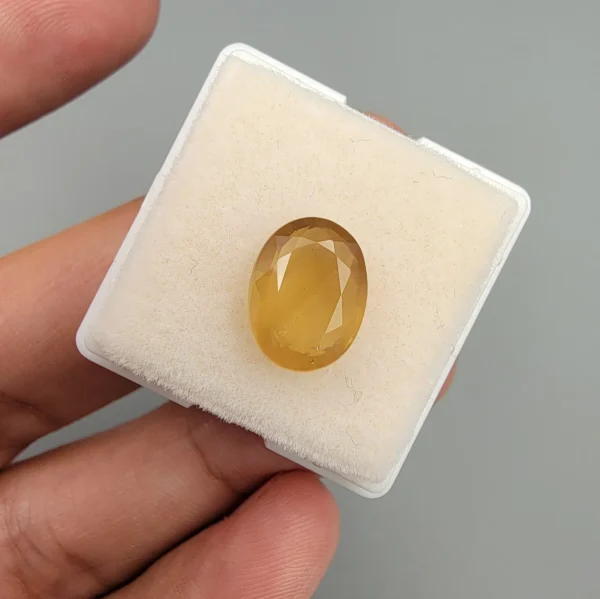 High-resolution macro photograph displaying a 3.78-carat natural Yellow Sapphire (Pukhraj) oval faceted gemstone held securely in gemological tweezers, featuring a warm golden-yellow body color, natural crystal inclusions, and brilliant facet architecture.