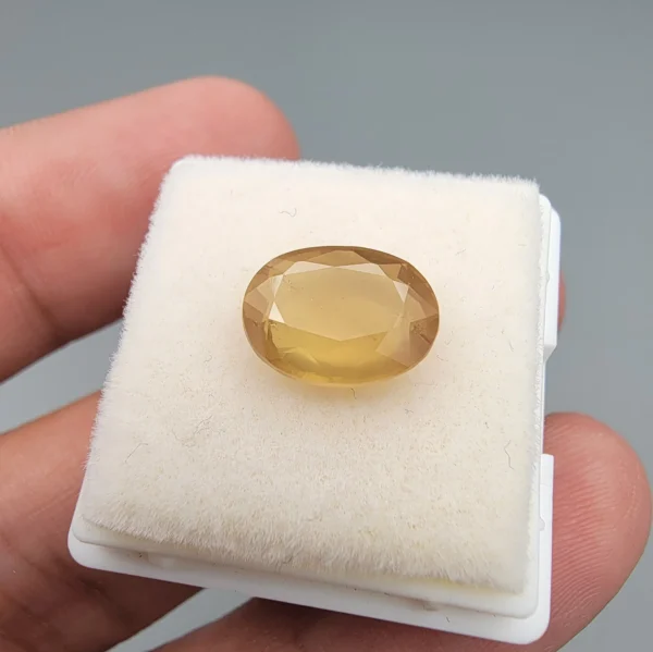 High-resolution macro photograph displaying a 3.78-carat natural Yellow Sapphire (Pukhraj) oval faceted gemstone held securely in gemological tweezers, featuring a warm golden-yellow body color, natural crystal inclusions, and brilliant facet architecture.