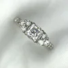 Multi-angle macro photographs of a 14K white gold 7-stone diamond engagement ring held against a white fabric backdrop, featuring a central natural cushion-cut diamond flanked by six graduated round brilliant-cut diamonds across the gallery band.