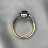 Close-up photograph of an 18K gold ring featuring a 1.53-carat emerald-cut pastel blue natural Ceylon sapphire centerpiece surrounded by a shimmering halo of 0.33-carat natural diamond accents against a soft white fabric background.
