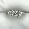 Multi-angle macro photographs of a 14K white gold 7-stone diamond engagement ring held against a white fabric backdrop, featuring a central natural cushion-cut diamond flanked by six graduated round brilliant-cut diamonds across the gallery band.