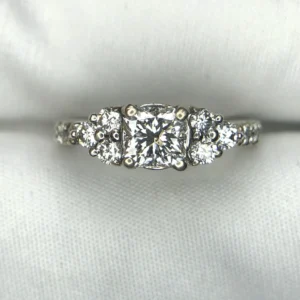 Multi-angle macro photographs of a 14K white gold 7-stone diamond engagement ring held against a white fabric backdrop, featuring a central natural cushion-cut diamond flanked by six graduated round brilliant-cut diamonds across the gallery band.