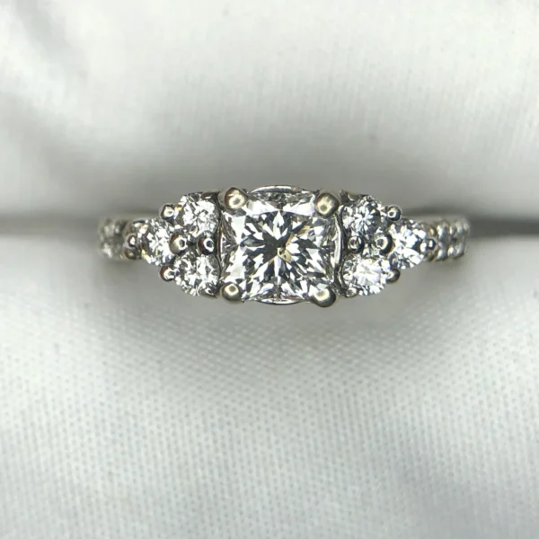 Multi-angle macro photographs of a 14K white gold 7-stone diamond engagement ring held against a white fabric backdrop, featuring a central natural cushion-cut diamond flanked by six graduated round brilliant-cut diamonds across the gallery band.